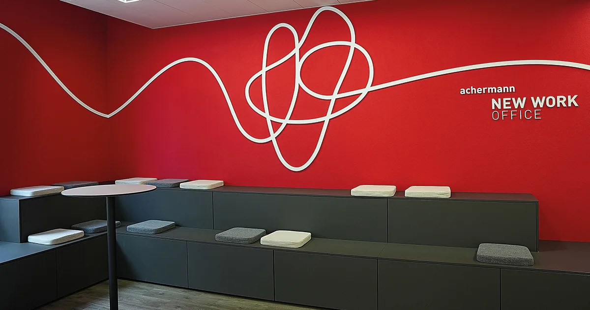 «New Work»: Die Achermann ICT Services AG hat ihren Sitz von Männedorf nach Rüti verlegt. Eine lederne Sitzgruppe vor einer knallroten Wand mit einer weissen Verzierung und der Aufschrift Achermann New Work Office.
